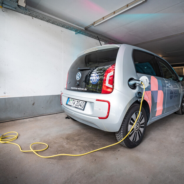 Blick auf ein E-Auto das gerade über ein LAdekabel aufgeladen wird. Das Auto steht in einer Tiefgarage