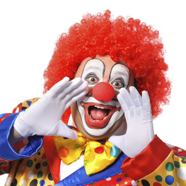 EIn Clown mit roter Perücke und buntem Kostüm hält die Hände vor den Mund als ob er laut etwas rufen würde.